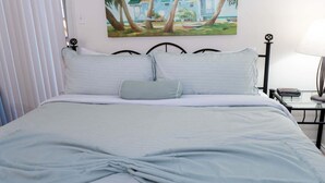 A neatly made bed with a grey duvet, a single pillow, and a decorative knot at the foot of the bed. There is a painting of a beach scene on the wall behind the bed. - Renovated 1st Floor Beach 250ft Pool 2 Bedroom Apts (South Padre Island)