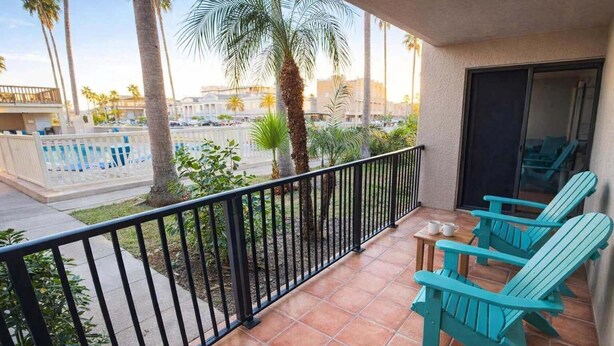 A balcony with a view of a pool, palm trees, and a building in the background. - Renovated 1st Floor Beach 250ft Pool 2 Bedroom Apts (South Padre Island)