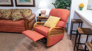 A living room with a red sofa, a wicker chair with a footrest, a small table with a lamp, and a green plant. - Renovated 1st Floor Beach 250ft Pool 2 Bedroom Apts (South Padre Island)
