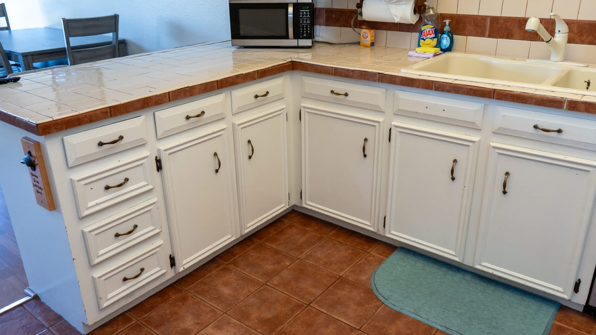 A kitchen with white cabinets, a microwave, a sink, and a green rug.