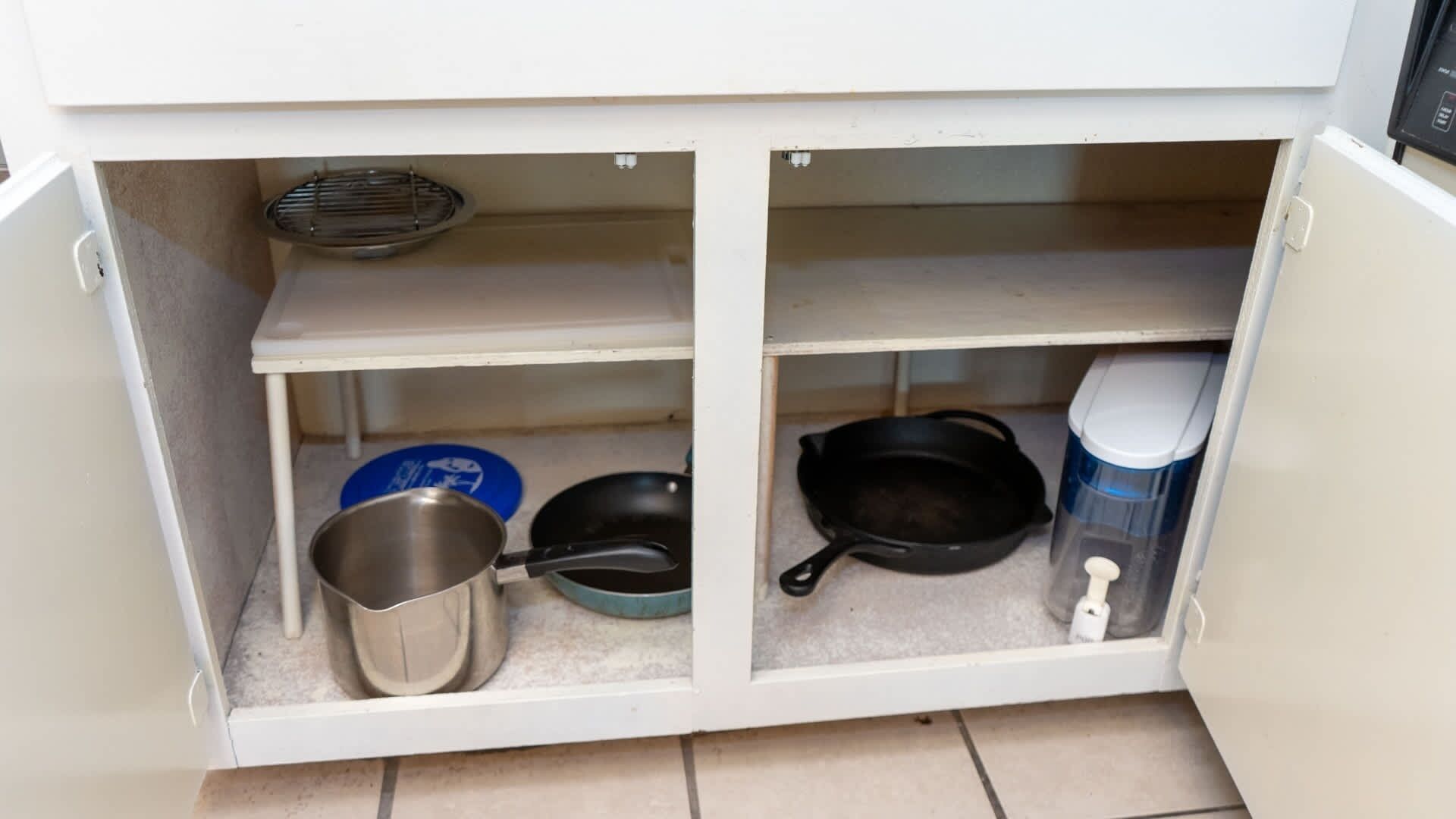 A kitchen cabinet with a metal pot, a frying pan, and a coffee maker.
