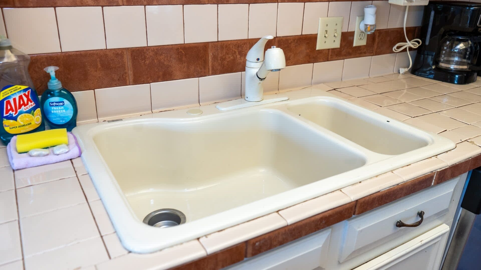 A kitchen with a double sink, a coffee maker, and cleaning supplies on the counter.