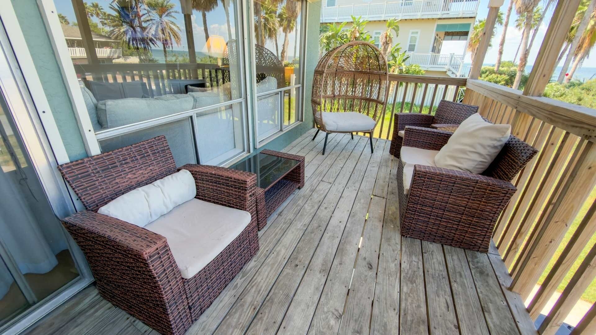 A covered outdoor seating area with wicker furniture and a glass enclosure.