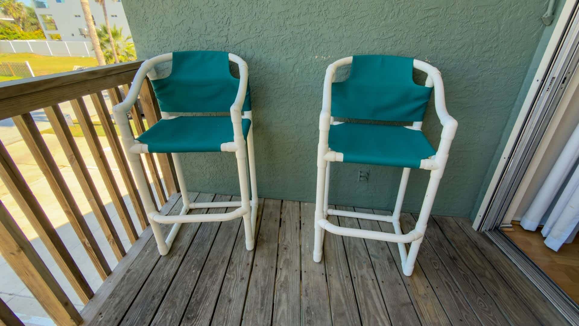 Two white chairs with teal cushions on a wooden deck.
