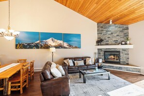 A living room with a fireplace, wooden ceiling, and a dining area with a table and chairs. - Candlelight Meadows Escape | Hot Tub Near Town Center & Spacious Great Room (Big Sky)