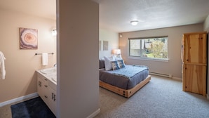 Ein Schlafzimmer mit Bett, Fenster, Holzschrank und einem Badezimmer mit Waschbecken und Handtuchhalter.