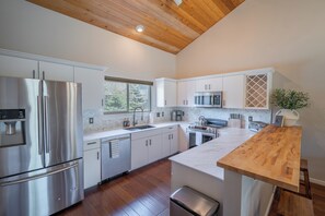 A modern kitchen with stainless steel appliances, white cabinetry, and a wooden ceiling. - Candlelight Meadows Escape | Hot Tub Near Town Center & Spacious Great Room (Big Sky)
