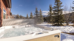 Ein Whirlpool mit Bedienfeld, umgeben von Schnee und Bäumen.