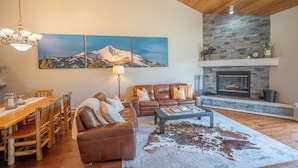 Ein Wohnzimmer mit Kamin, einem Essbereich mit Holztisch und Stühlen sowie einem großen Wandbild einer Berglandschaft.
