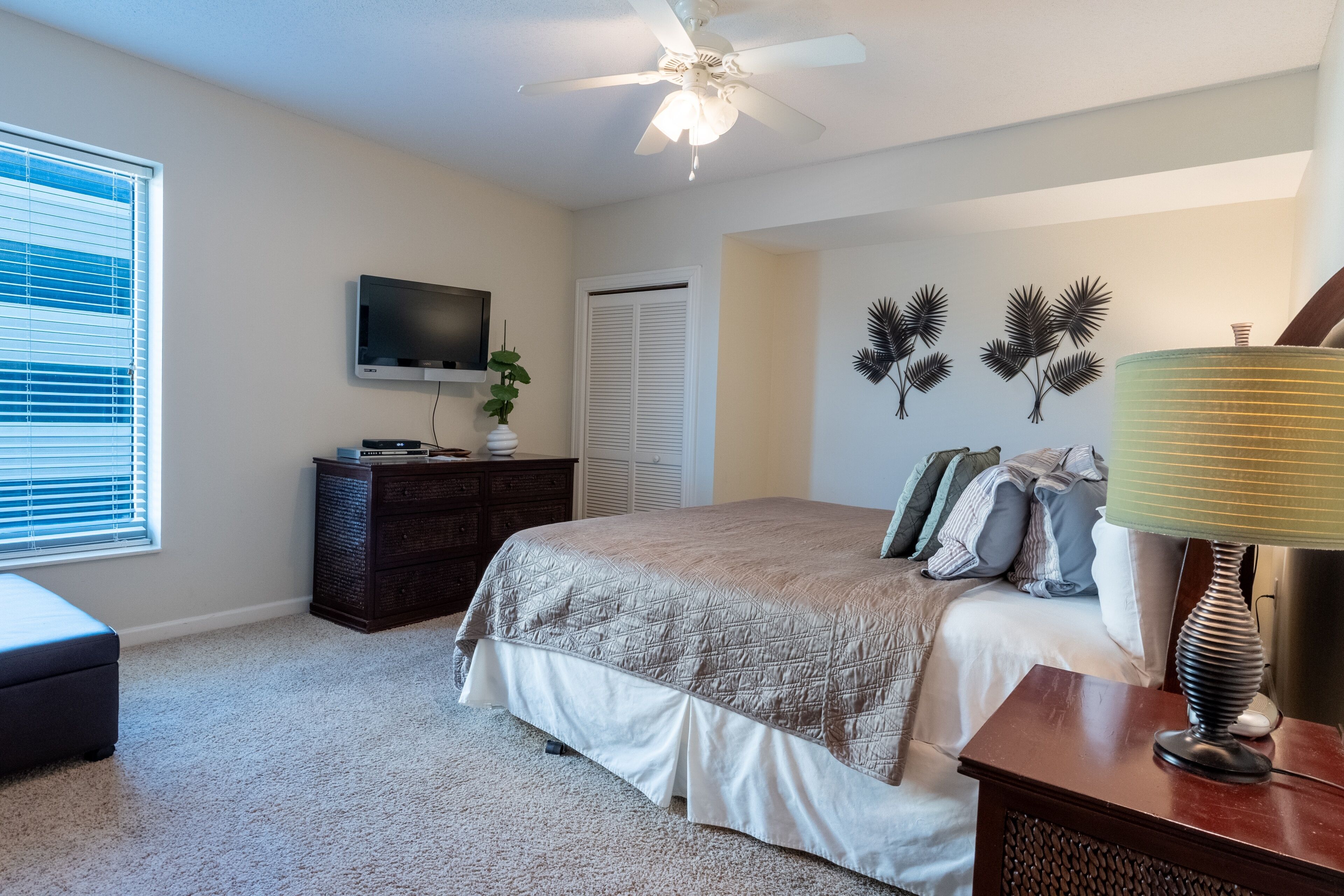 Ein Schlafzimmer mit Bett, Deckenventilator, Fernseher, Kommode und Lampe.