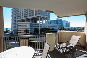 A balcony with a table and chairs, overlooking a modern building complex and a parking area. - 208 Royale Palms 3 Bedroom Condo (Myrtle Beach)
