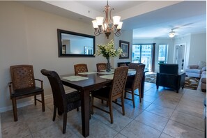 A dining area with a wooden table, six chairs, a chandelier, and a vase with flowers. - 208 Royale Palms 3 Bedroom Condo (Myrtle Beach)