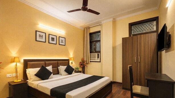 A hotel room with a large bed, bedside lamps, a ceiling fan, a TV, a wardrobe, and a window with a view. - A Square Homes & Stay (New Delhi)