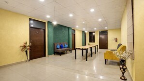 A hotel lobby with a reception desk, seating area, and a plant. - A Square Homes & Stay (New Delhi)