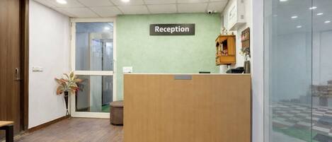 A reception area with a wooden desk, a reception sign, a potted plant, and a glass door leading outside.