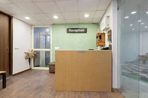 A reception area with a wooden desk, a reception sign, a potted plant, and a glass door leading outside.