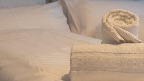 Un lit bien fait, avec des draps blancs et une serviette enroulée, une tête de lit décorative et un oreiller.