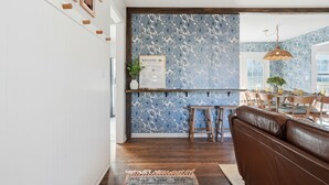 Eine moderne Küche mit blauer Blütenrückwand, Holzbarhocker und einem Willkommen-Schild.