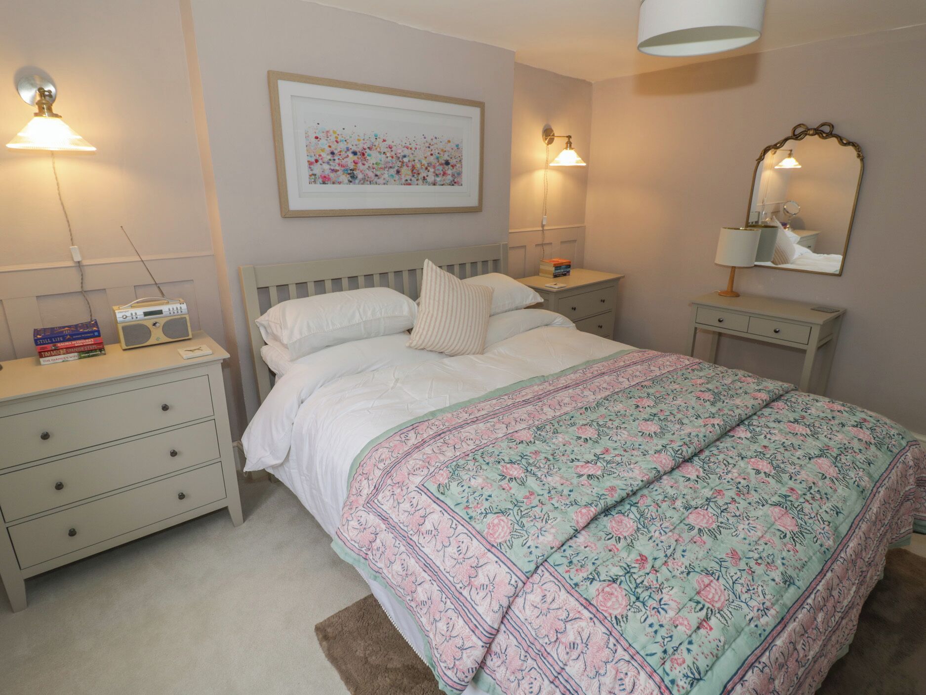 A neatly arranged bedroom with a bed, bedside tables, a radio, and a framed picture on the wall.