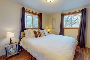 A neatly made bed with white bedding and brown pillows, two bedside lamps, a wooden nightstand with a tissue box, and a window with curtains.