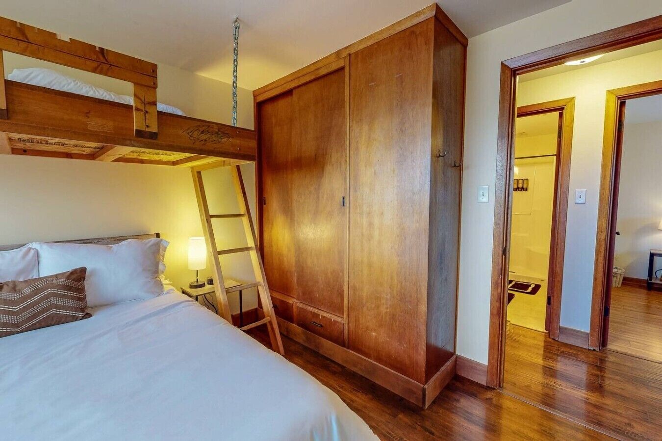 A bunk bed with a ladder, a wardrobe, and a bathroom door.