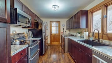 A kitchen with dark wood cabinets, stainless steel appliances, a granite countertop, and a wooden floor.