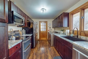 A kitchen with dark wood cabinets, stainless steel appliances, a granite countertop, and a wooden floor.