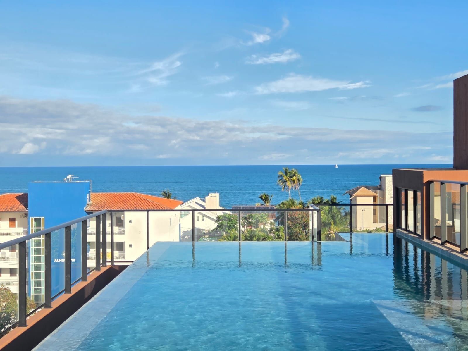Una piscina infinita en la azotea con vista al océano y palmeras.