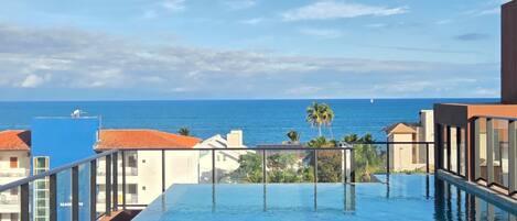 Una piscina infinita en la azotea con vista al océano y palmeras.