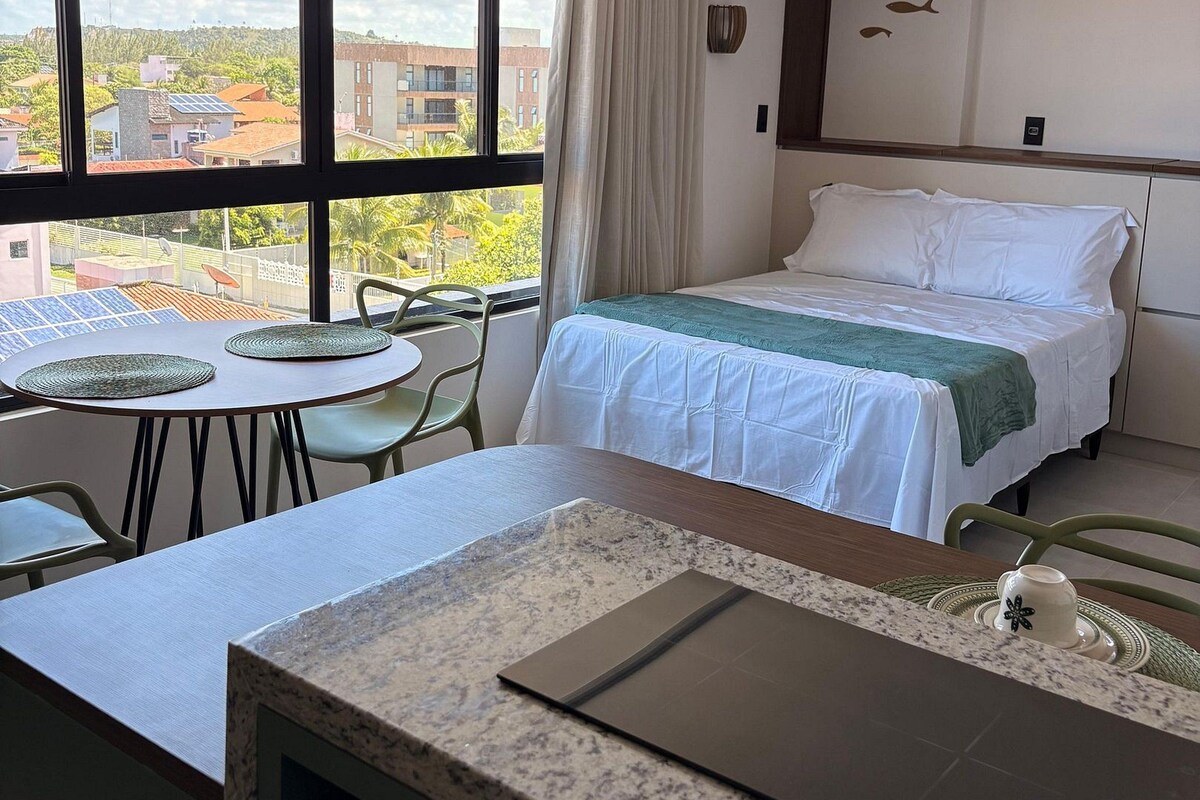 Ein Hotelzimmer mit einem Bett, einem Schreibtisch mit einem Laptop, einem Esstisch und Blick auf die Stadt durch große Fenster.
