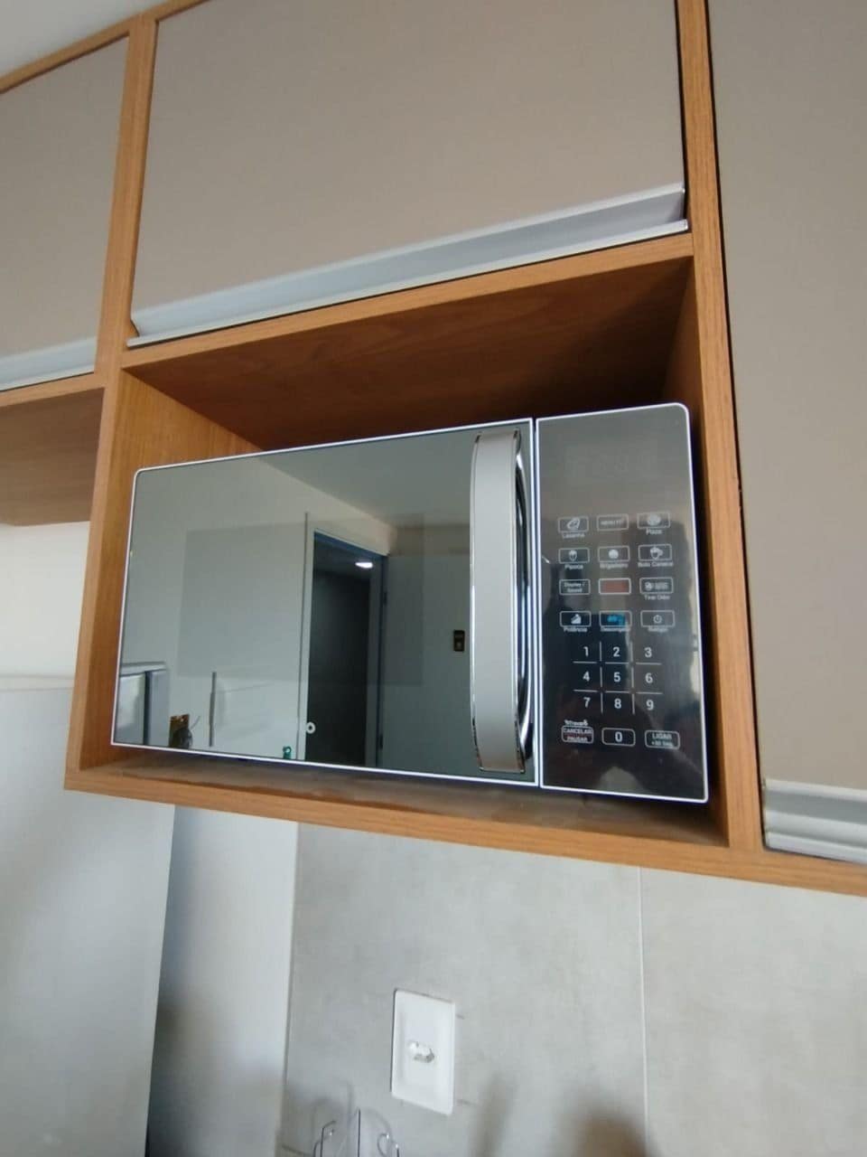 Eine eingebaute Mikrowelle mit digitaler Bedienkonsole, untergebracht in einem Holzschrank mit spiegelglänzender Tür.
