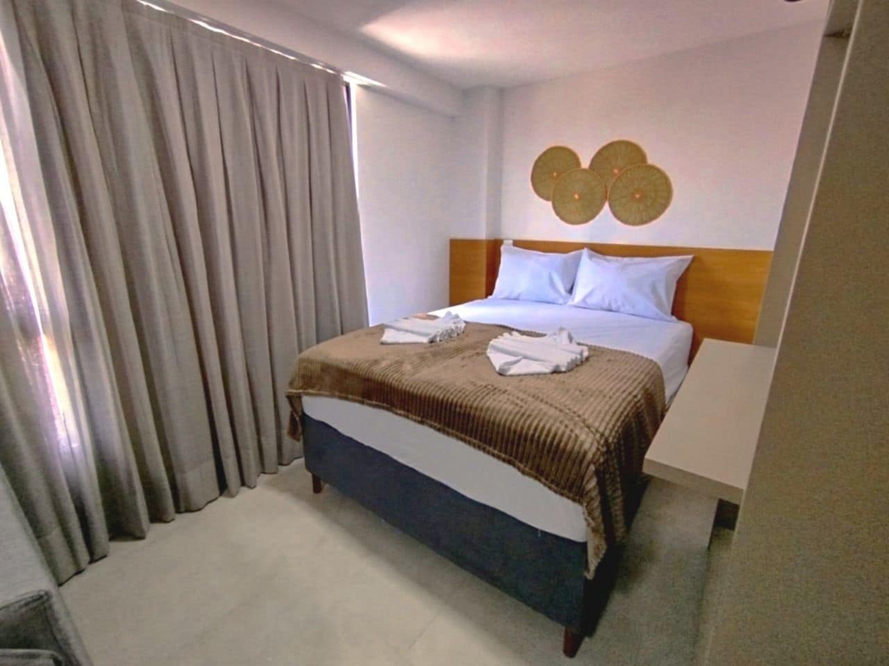 A hotel room with a bed, curtains, a headboard, and a wall decoration.
