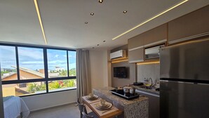 A modern kitchen with a large window, a dining area, and a built-in refrigerator. - Carneiros Beach Exclusive (Tamandaré)