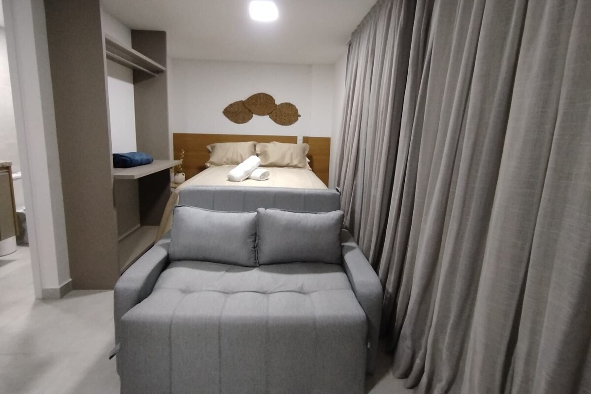 A modern hotel room with a bed, a seating area, and a shower.