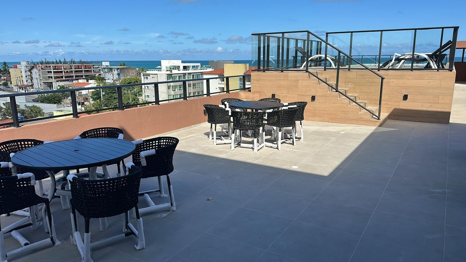 A rooftop terrace with outdoor seating, a staircase, and a view of the ocean and buildings.