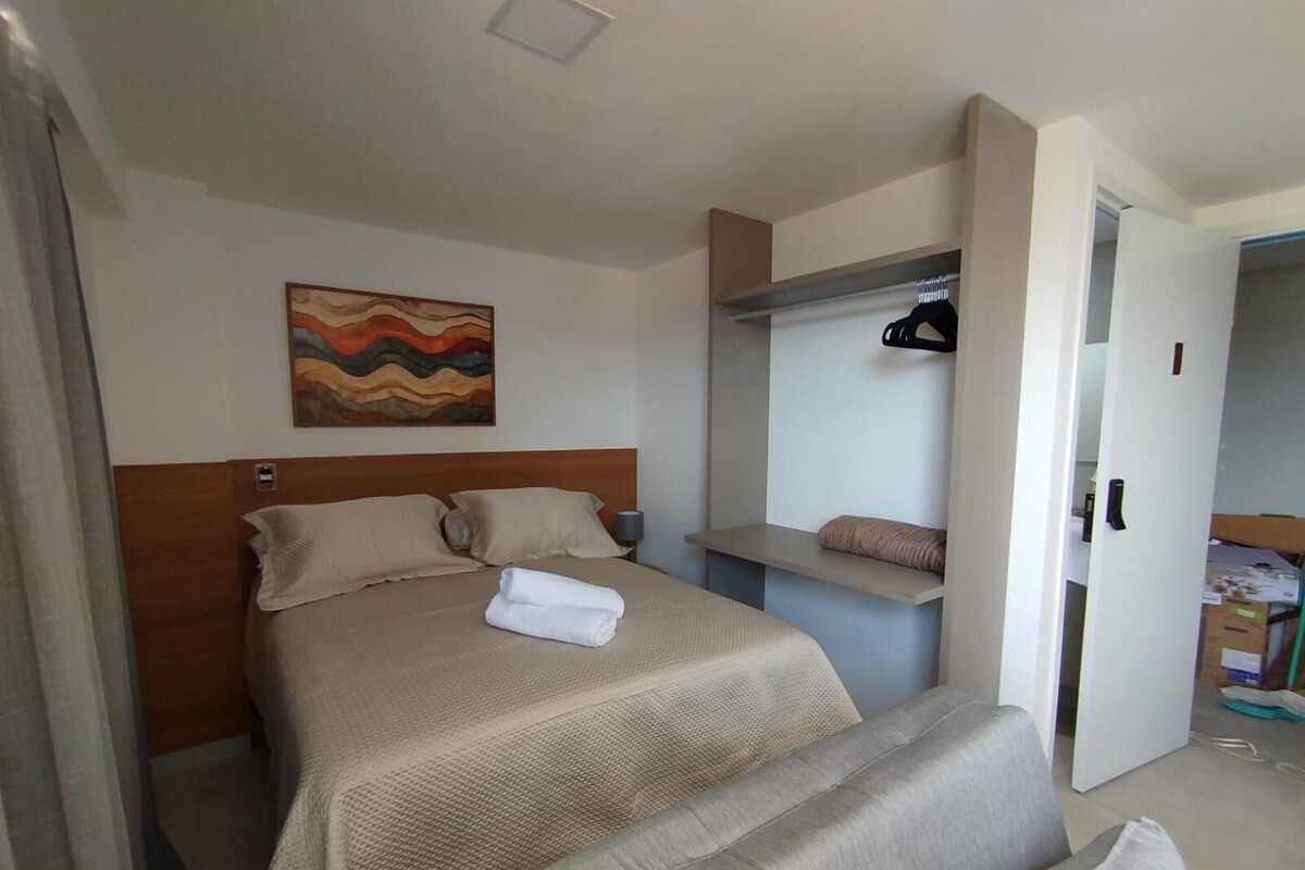 A hotel room with a bed, a painting on the wall, a bedside table, and a wardrobe.
