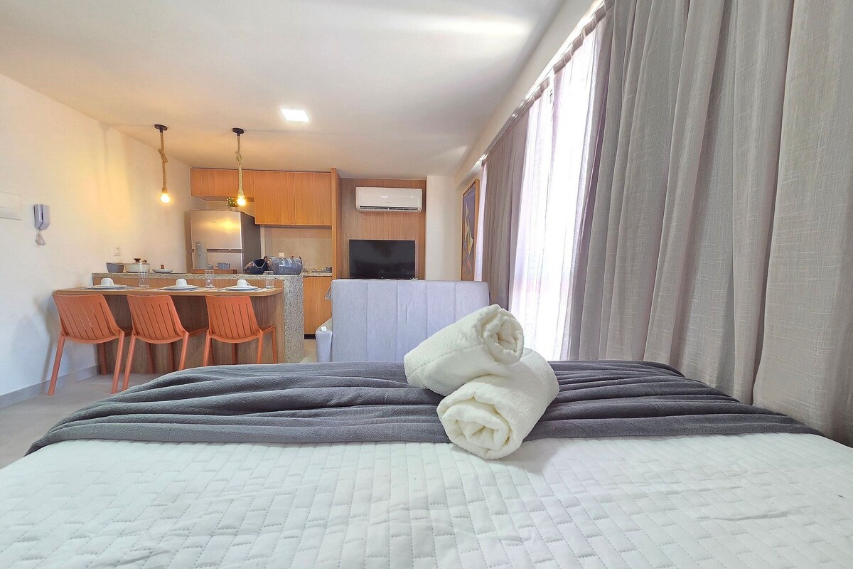 A hotel room with a bed, a small kitchenette, a dining area, and a TV.