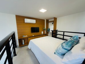 Ein Hotelzimmer mit einem Bett, einem an der Wand befestigten Fernseher, einem Nachttisch und einem kleinen Regal mit einer Pflanze.