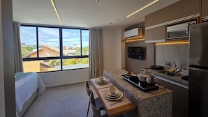 A modern kitchen with a large window, a dining area, and a bed. - Carneiros Beach Exclusive (Tamandaré)