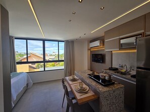 A modern kitchen with a large window, a dining area, and a bed. - Carneiros Beach Exclusive (Tamandaré)