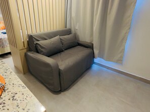 A grey sofa in a room with a wooden partition and a white curtain. - Carneiros Beach Exclusive (Tamandaré)