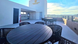 A rooftop terrace with a table and chairs, a small kitchenette, and a view of the city. - Carneiros Beach Exclusive (Tamandaré)