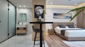 A modern bedroom with a large bed, a desk with a chair, a nightstand, and a wall-mounted TV. - Elegant Suites in the Heart of Piraeus (Piraeus)