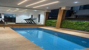 Ein Hallenbad mit Holzterrasse, Fitnessgeräten und einer grünen Wand mit Pflanzen.