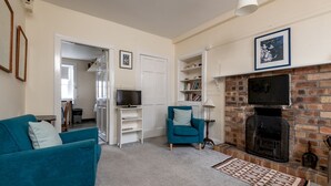 A living room with a blue sofa, a television, a fireplace, and a bookshelf. - South Street (No 16A) | Elie (Elie)