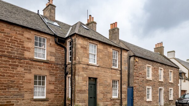 A row of stone buildings with multiple windows and doors, a visible street, and a parked car. - South Street (No 16A) | Elie (Elie)