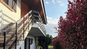 A modern building with a staircase leading to a balcony, surrounded by lush greenery and red foliage. - Alma CaloRosa – Sea View Escape in Romantic Moledo, Northern Portugal (Moledo)