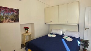 Een slaapkamer met een bed, witte kasten, een klein tafeltje met een bloemenvaas en een wandairconditioner.