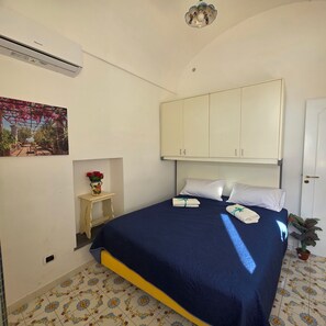 A bedroom with a bed, white cabinets, a small table with a vase of flowers, and a wall-mounted air conditioner. - ALMARY HOUSE WITH SEA VIEW (Amalfi)