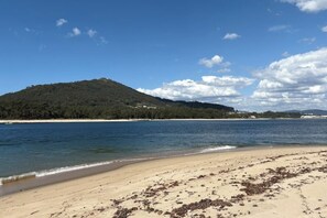 Ein Strand mit sandigem Ufer und einer Hügelkette im Hintergrund.